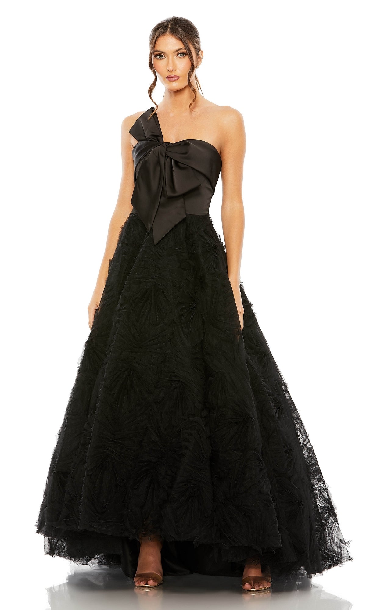 A woman stands against a white background wearing the Long Formal Dress 20584 by Mac Duggal—a black A-line gown featuring a striking bow detail on the bodice and a full, textured skirt.